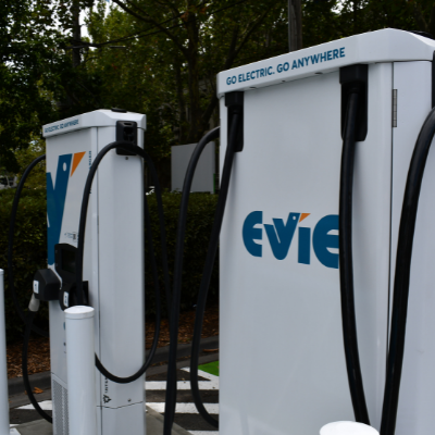 White electric vehicle chargers in foreground with trees behind