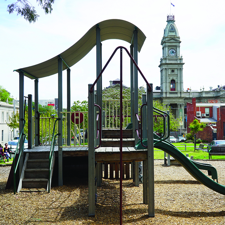 A playground with a wave-shaped roof and a clock tower in the background