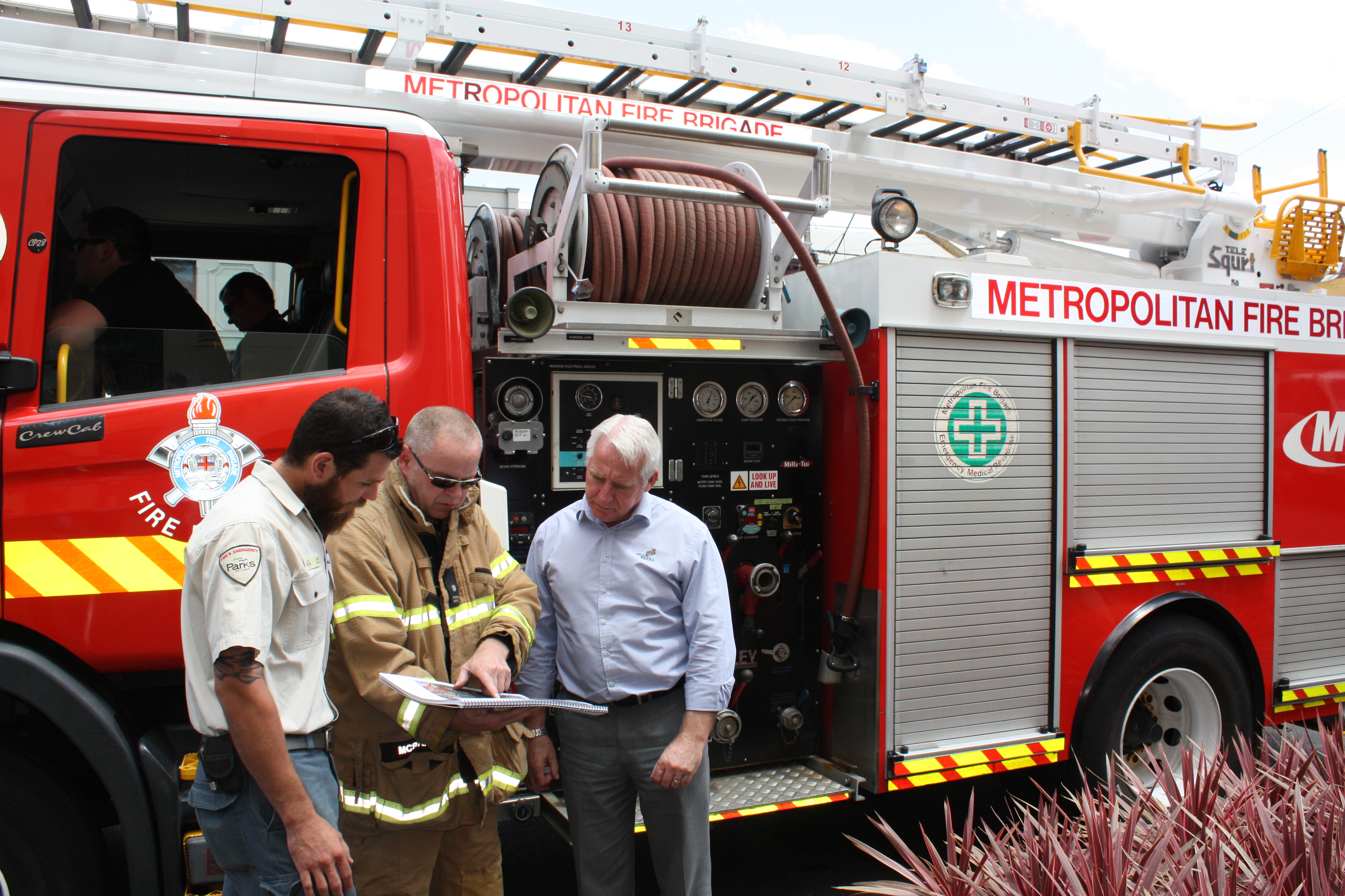 Three men looking at plans next to a fire truck