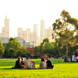 Group of people sitting on grass in park, with Melbourne CBD skyline in background