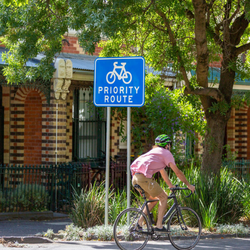 Cyclist wearing a helmet cycling on residential street, passing a sign saying priority route with an image of a bike