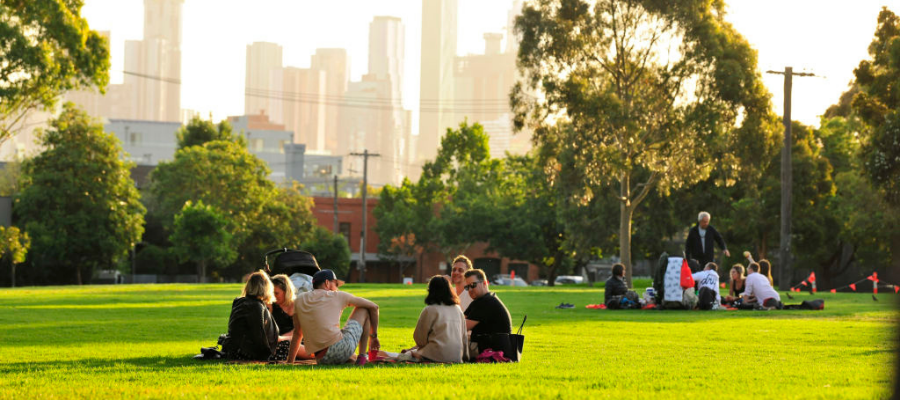 Group of people sitting on grass in park, with Melbourne CBD skyline in background