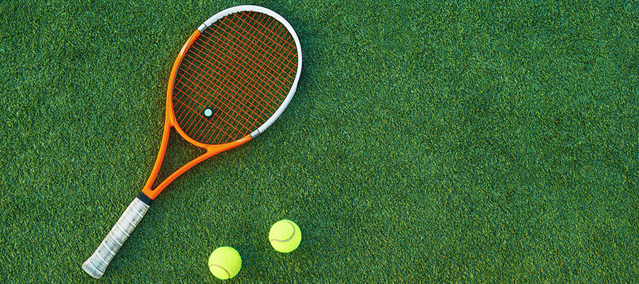 Tennis racquet and two balls lying on grass