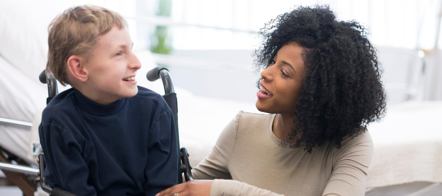 Child in wheelchair smiling at female carer
