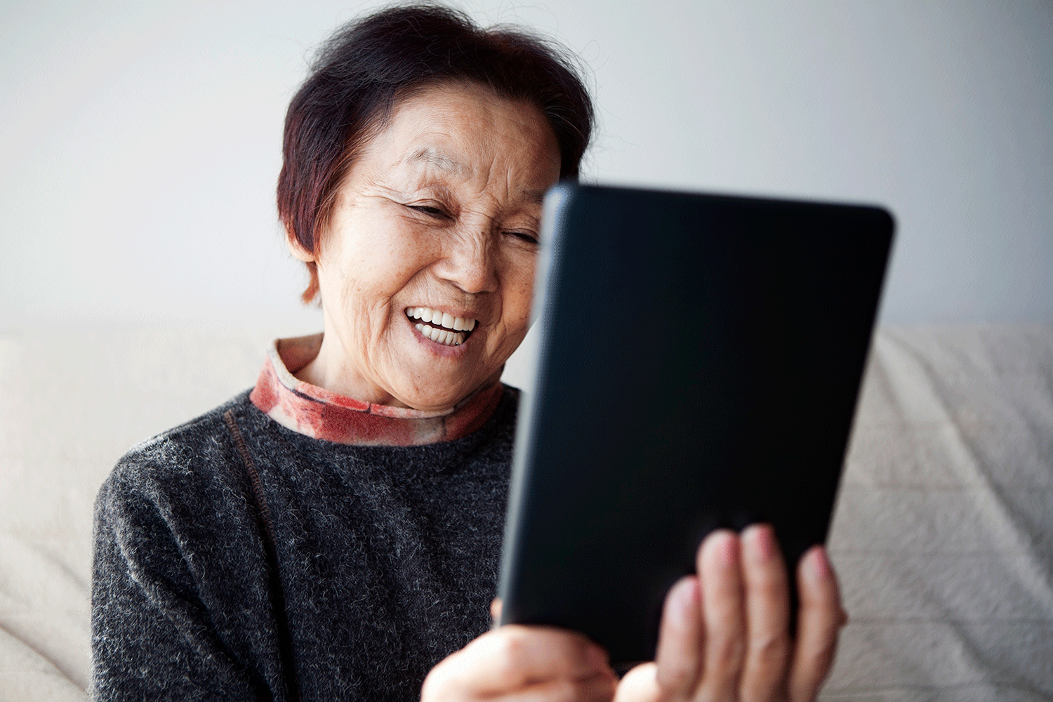 An older woman smiling a she chats to someone on a computer