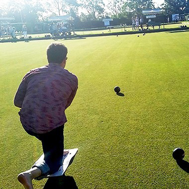 Man kneeling over bowling lawn bowl ball on greens