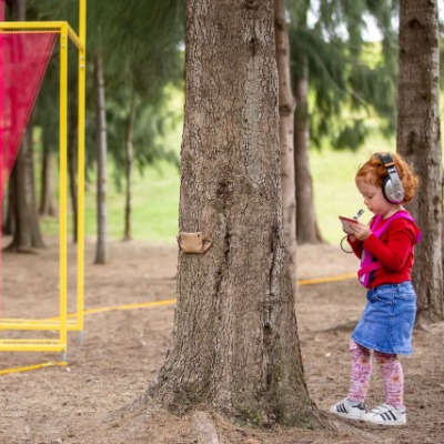A child wearing headphones and writing on a piece of paper while walking through a park