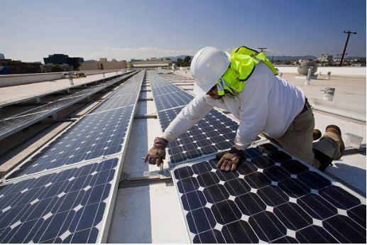 A tradesperson installing solar panels on a large rooftop