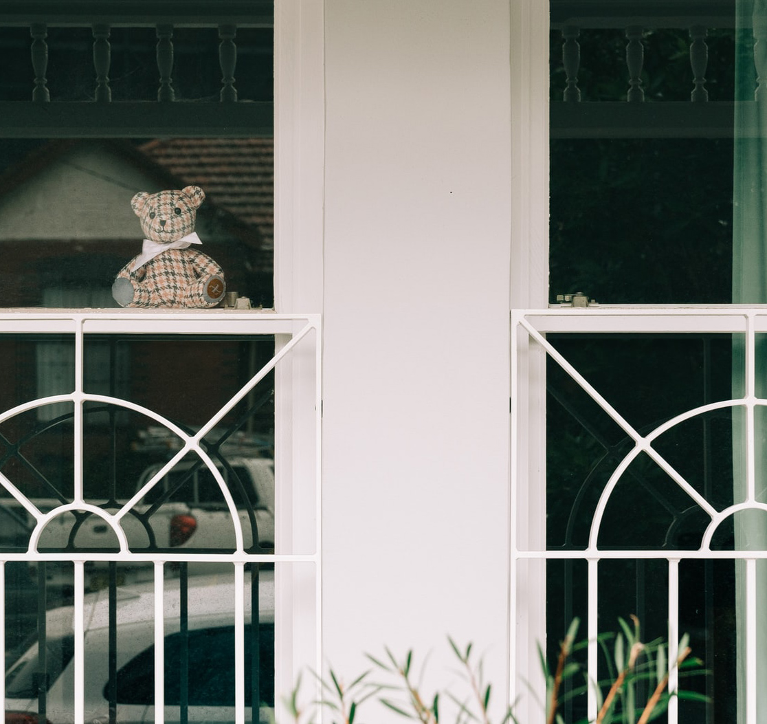 Photo of a teddy bear in a window on a white-painted house