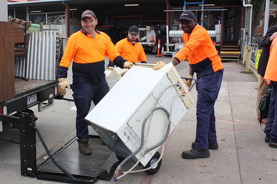 Two council workers moving fridge off collection trolley