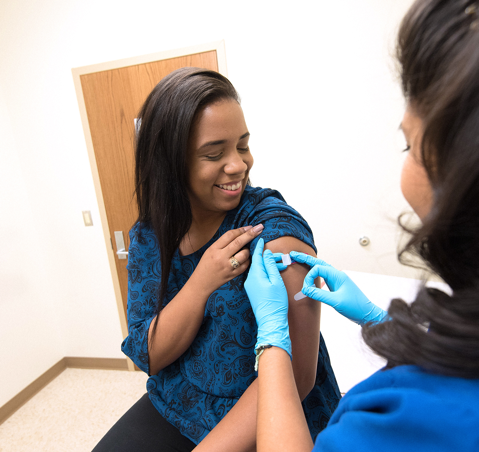 Image of a woman in a blue shirt receiving an immunisation from a health care worker