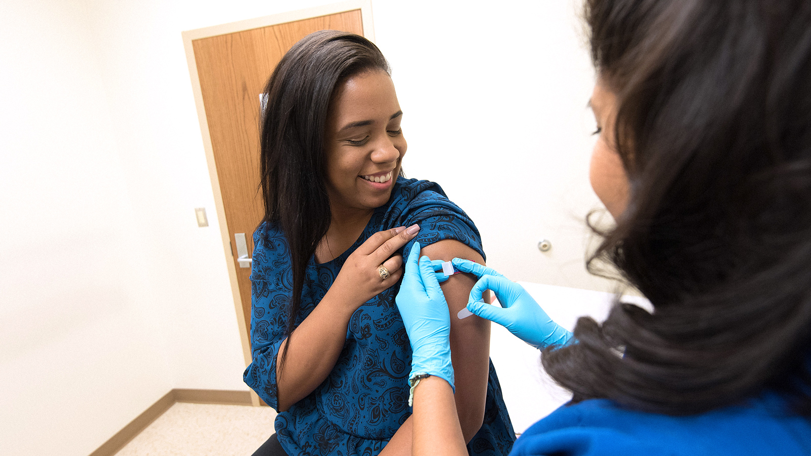 Image of a woman in a blue shirt receiving an immunisation from a health care worker