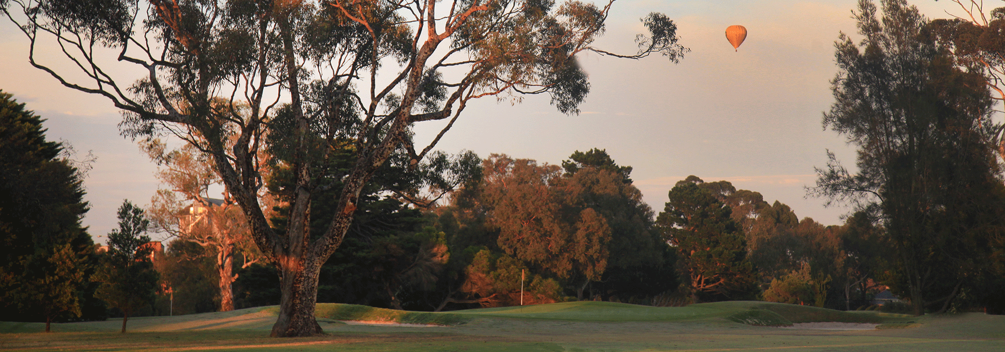 The golf course at sunrise with a hot air balloon in the distance