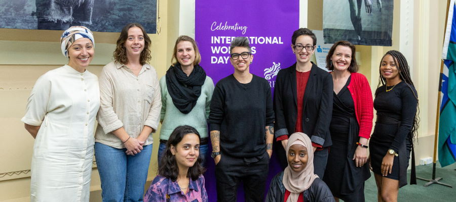 Group of women standing infront of a purple banner that says Celebrating International Women's Day