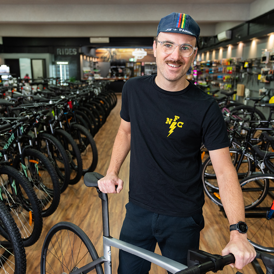 local trader smiling at camera while holing bicycle within bike store