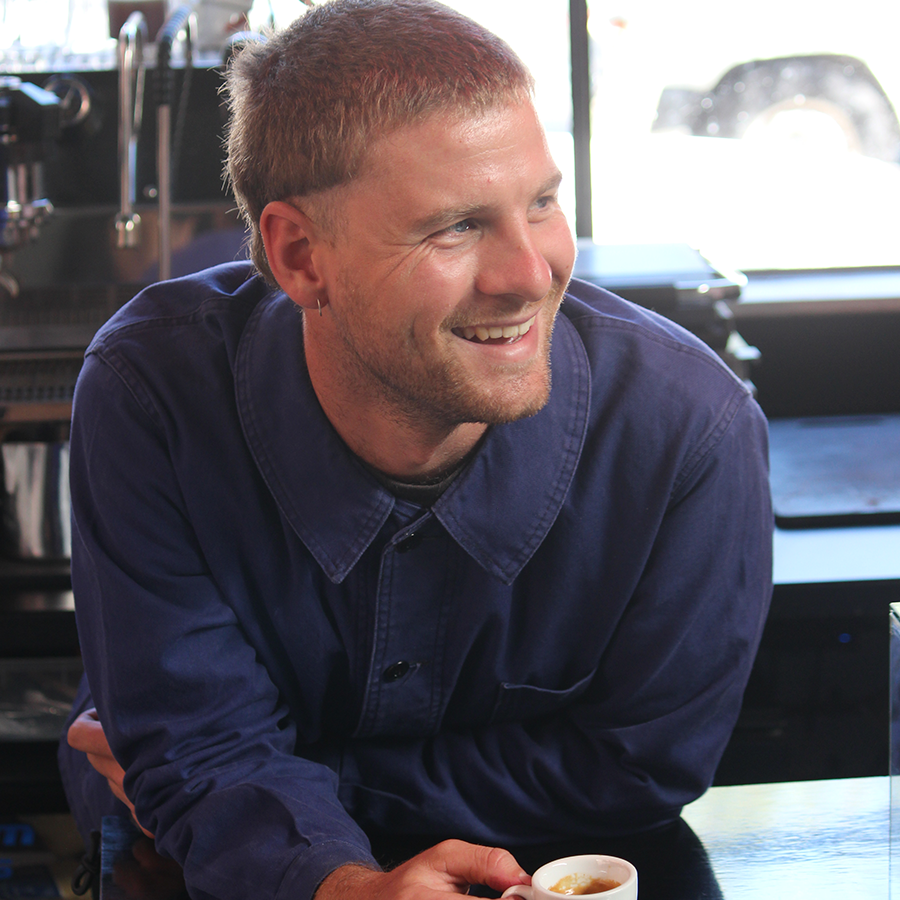 cafe owner leaning on bench with small cup of espresso