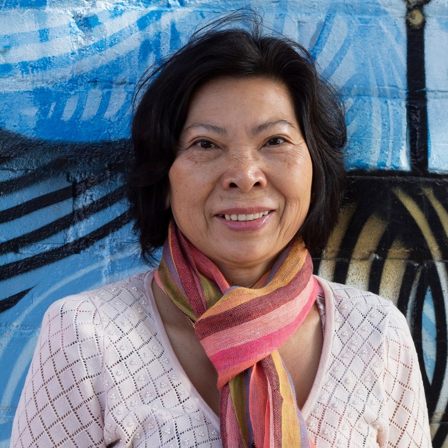 Asian woman with scarf smiling in front of painted brick wall 