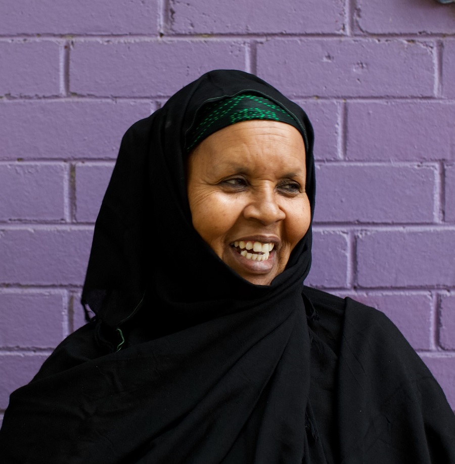 Woman in black veil smiling in front of purple painted brick wall