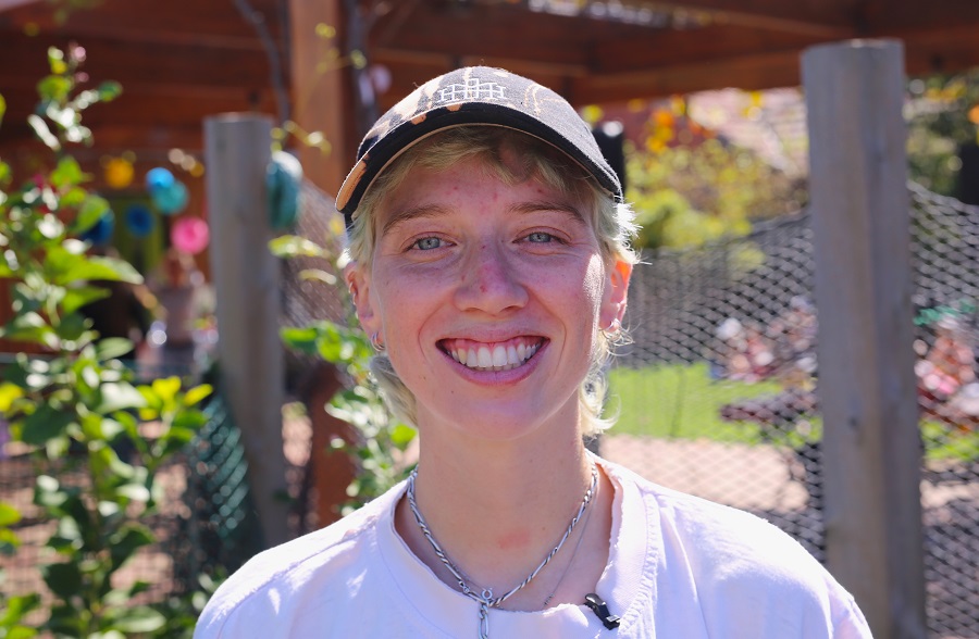 Girl with blond hair and a cap smiling with a community garden.