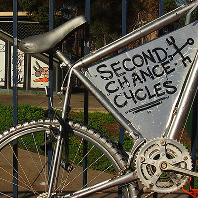 metal bicycle leaning against a fence engraved with second chance cycles