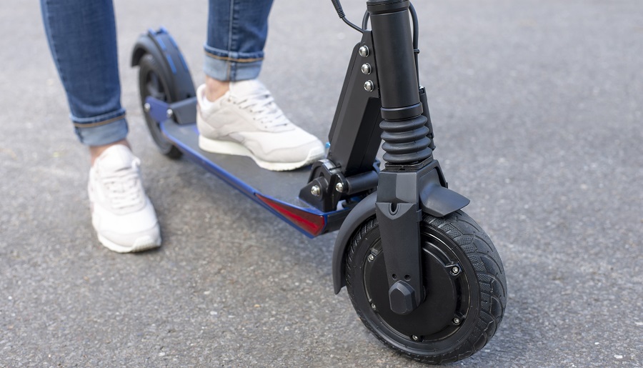 Person wearing jeans and sneakers getting on to an e-scooter