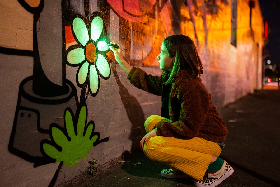 Teenager painting a flower mural on a wall with glow in the dark green paint