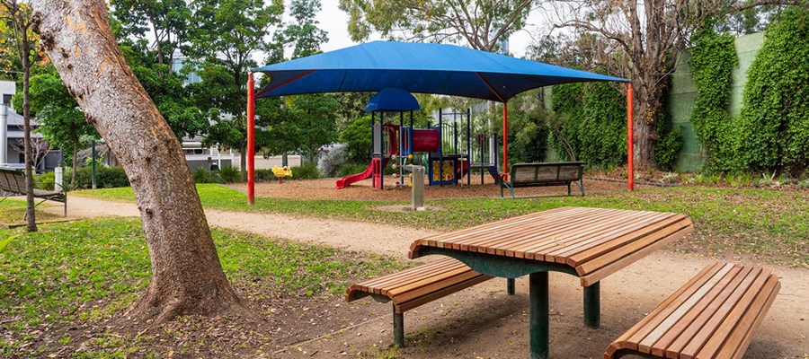 A small park with a playground, park bench and table and trees.