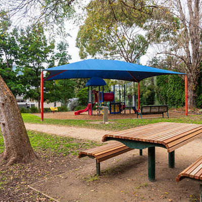 A small park with a playground, park bench and table and trees