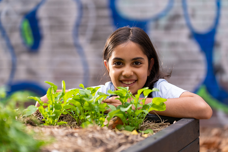 Smiling child behind plants growing in urban garden