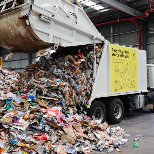 Recycling truck pouring out recycling contents onto warehouse floor 