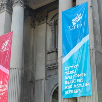 A blue banner with white text saying City of Yarra welcomes refugees and asylum seekers, hanging outside Fitzroy Town Hall