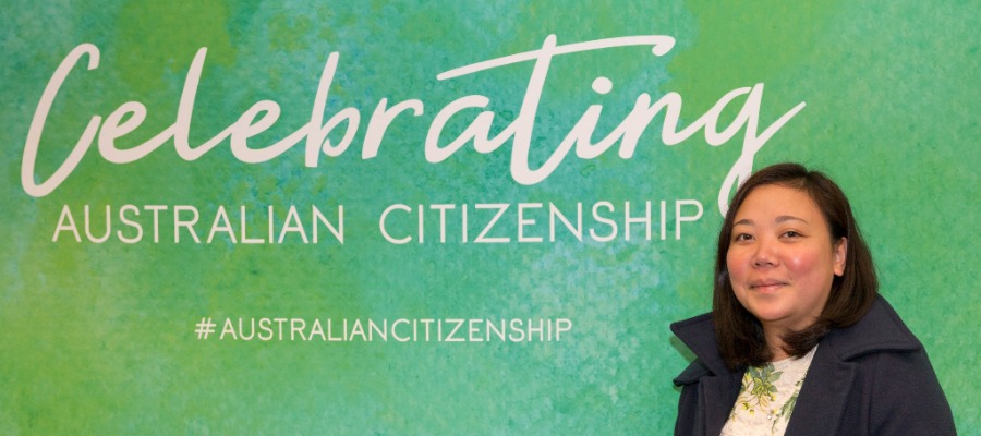 A person standing in front of a Celebrating Australian Citizenship banner