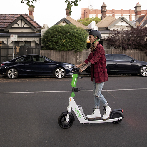 A young man with wondrous white boots riding an e-scooter down a Yarra sidestreet