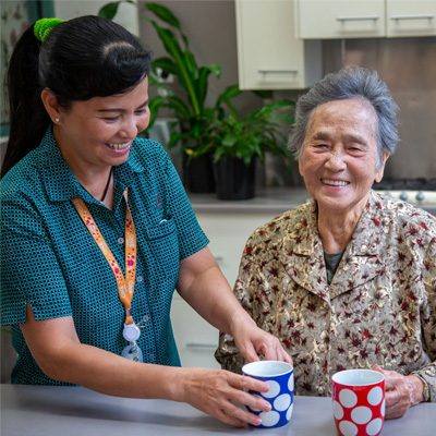 An elderly person smiles while a support worker helps her with something