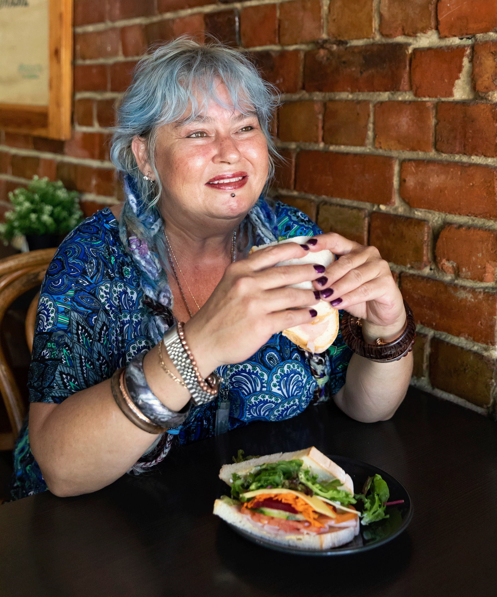 A woman in a cafe smiling and holding a sandwhich
