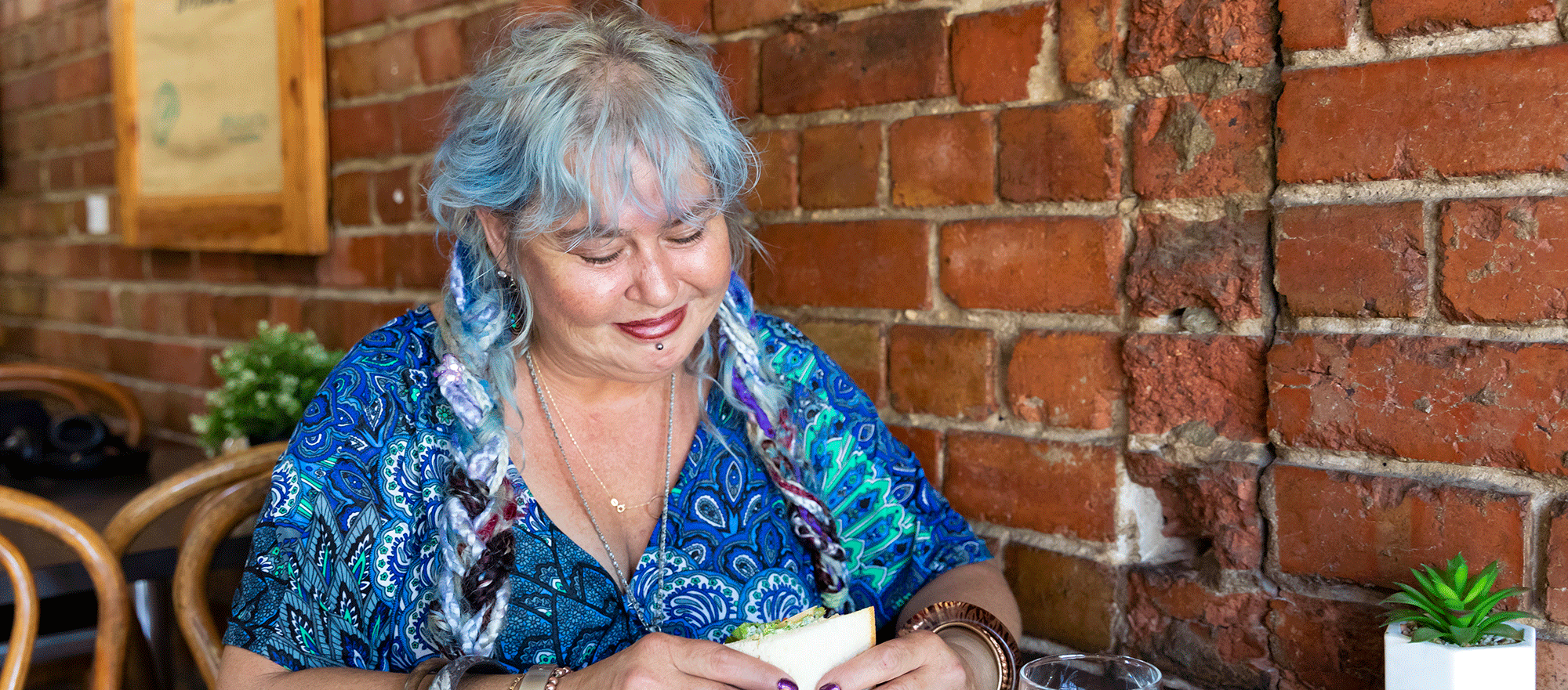 A woman in a cafe with exposed brick walls eating a sandwhich