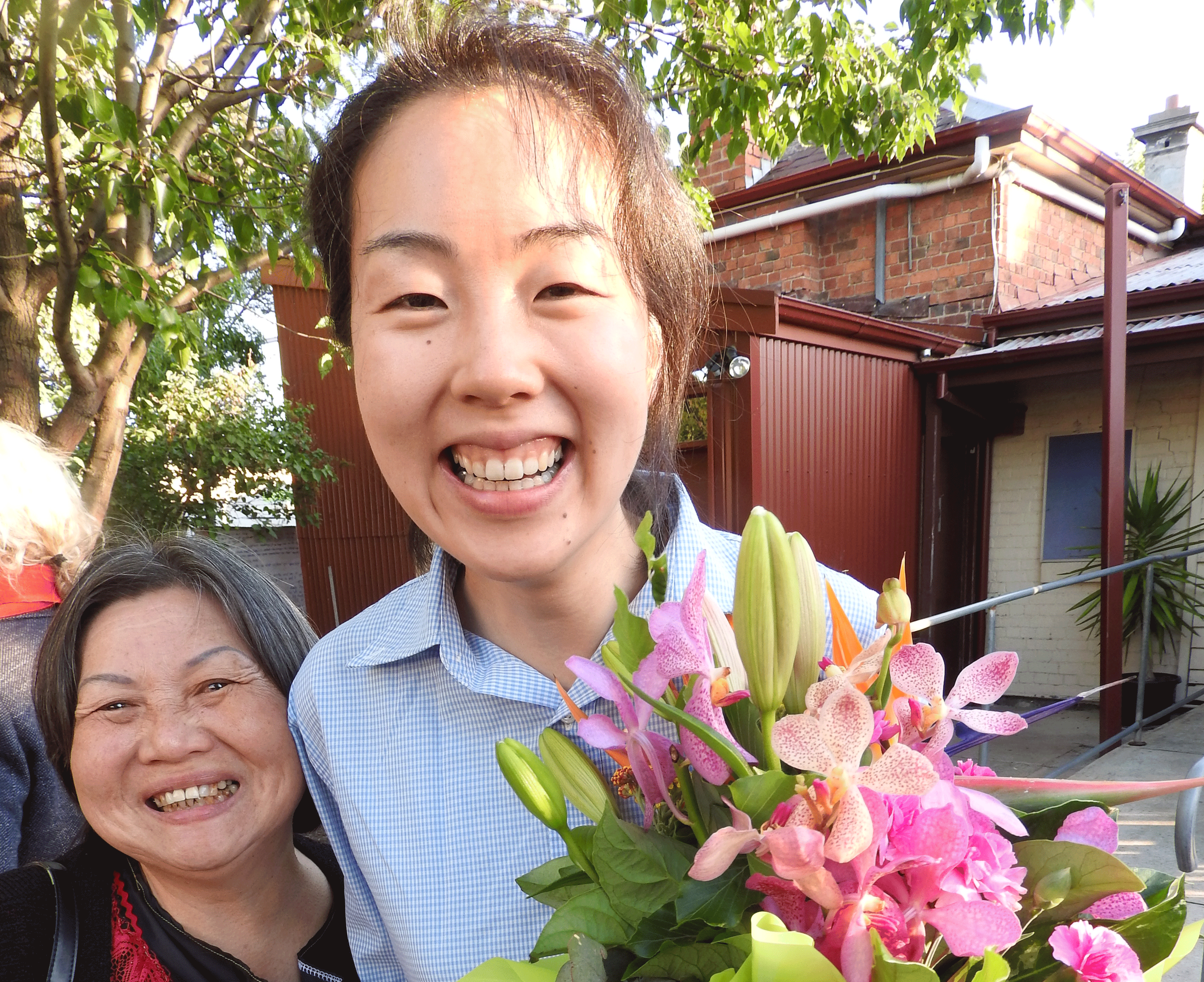 A young woman hugging an older woman and smiling with a bunch of flowers