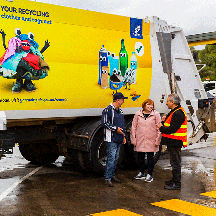 Three people smiling and chatting in front of a recycling truck