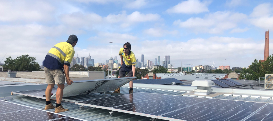 Two tradesmen installing solar panels on a roof on a cloudy day