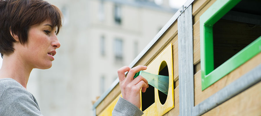 Photo of a woman putting a plastic bottle into a recylcing bin