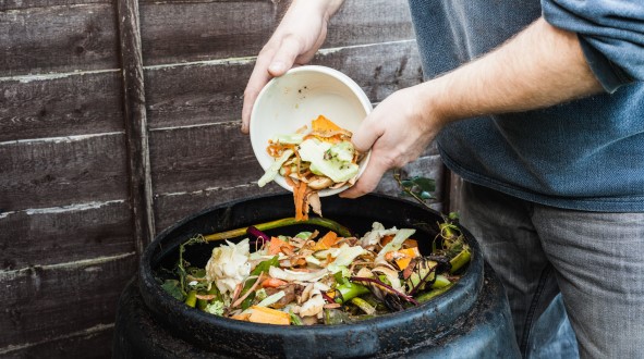 Person emptying colourful food scraps into a compost bin in front of a wooden fence.