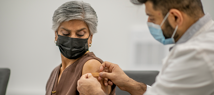 Older woman having a band aid placed on her arm by doctor after receiving a vaccination