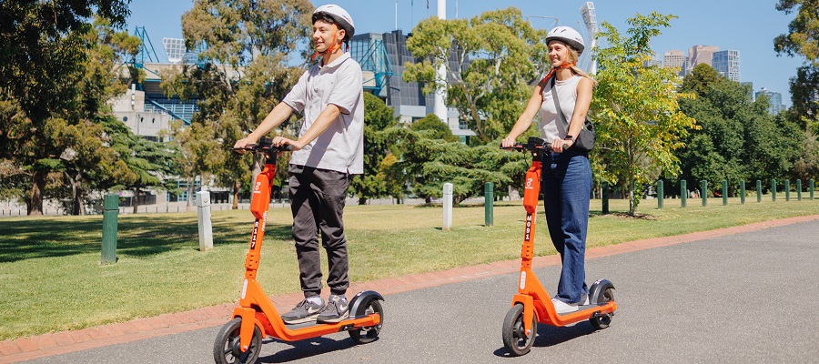 A amn and a woman riding bright orange e-scooters on a sunny day 