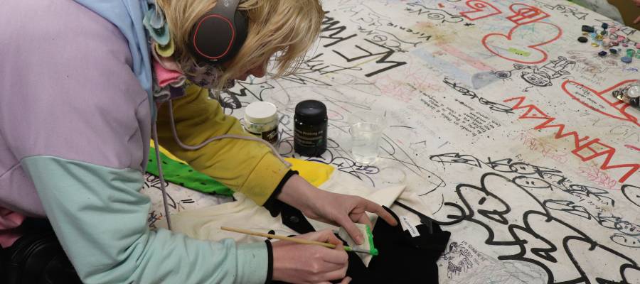 A young person leans over some artwork with a paint brush
