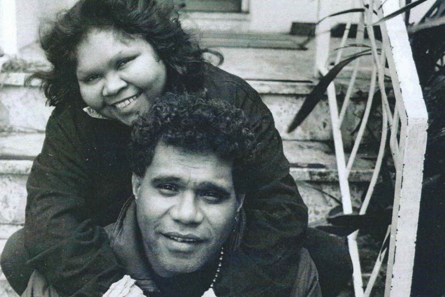 A black and white photograph of Ruby Hunter smiling with her arms around a smiling Archie Roach in 1990.