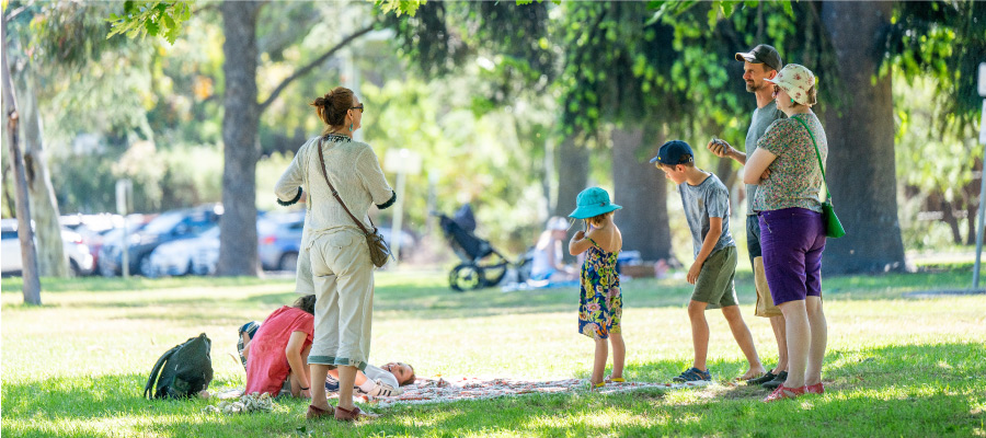 A group of adults and children stand in a sunny park