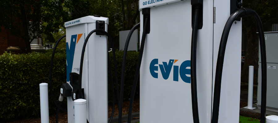 Two white electric vehicle chargers in foreground, in front of trees