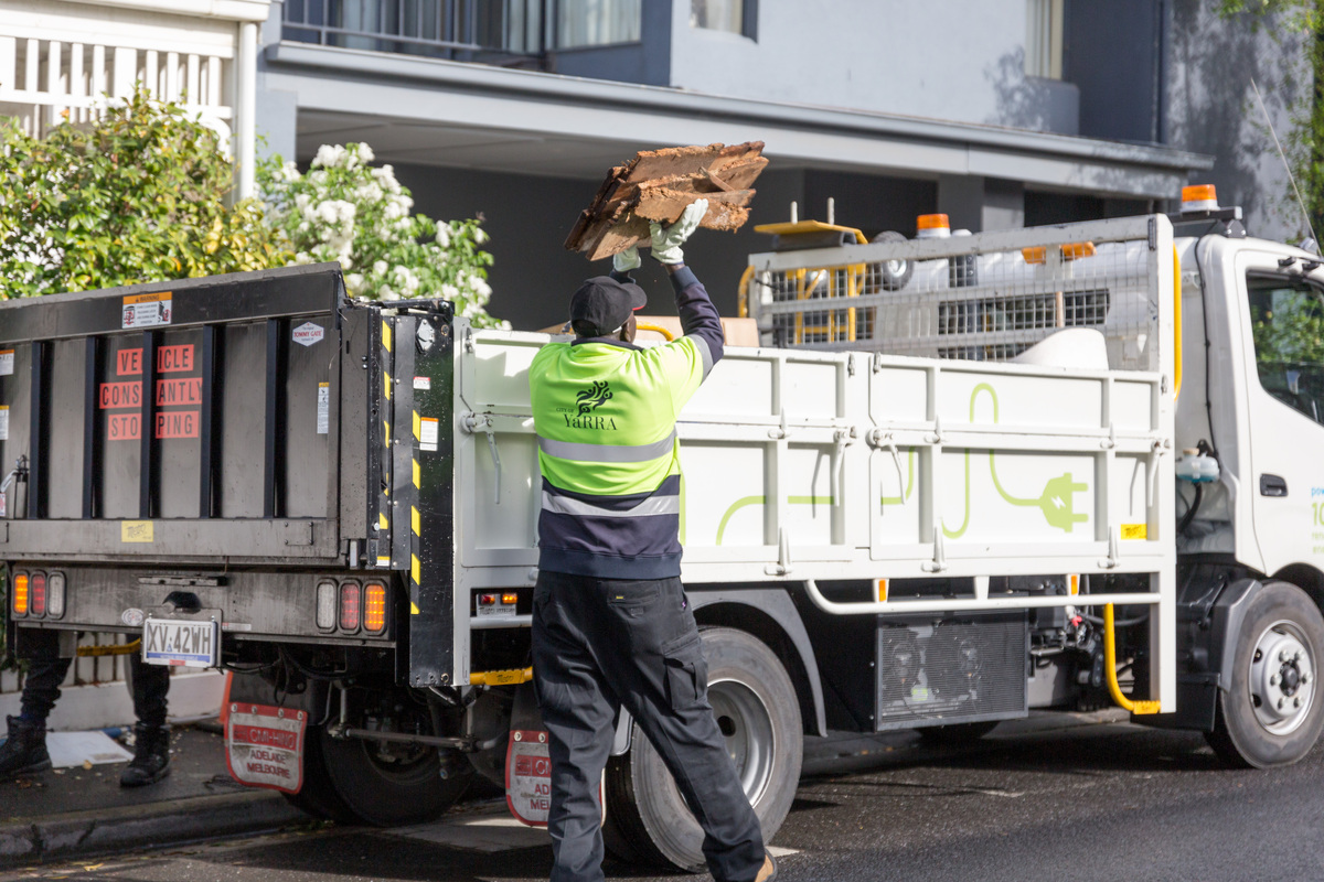 Yarra City Council workers collect waste from a residential street and load it into the back of an open-top truck. 