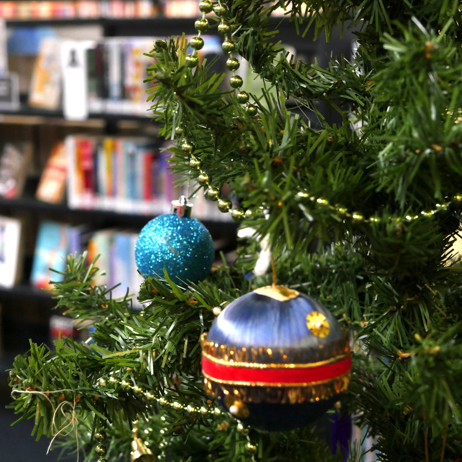 A fake Christmas Tree with blue and purple baubles, with library shelves in the background.  